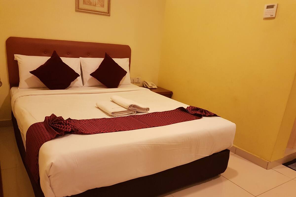 A neatly made bed with a red blanket, white linens, and two dark pillows.