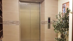 An elevator with a digital display, beige tiled walls, and a potted plant. - Sun Inns Hotel Bandar Puchong Utama (Puchong)