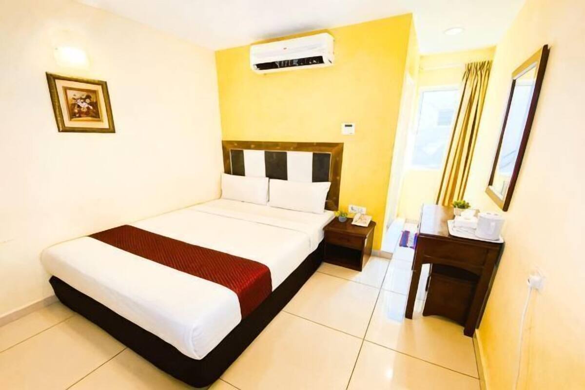 A hotel room with a bed, bedside table, nightstand, and a window with curtains.