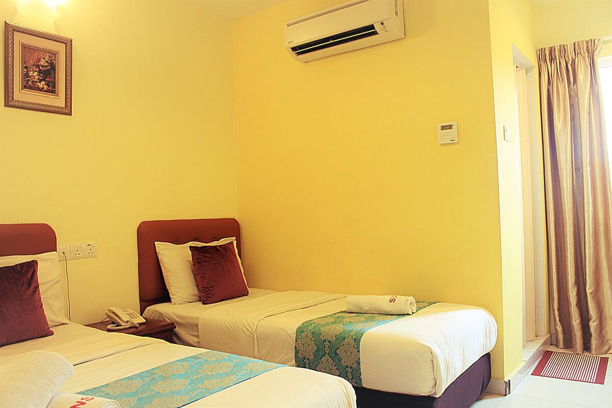 A hotel room with two beds, a wall-mounted air conditioner, a telephone, and a curtain on the window.