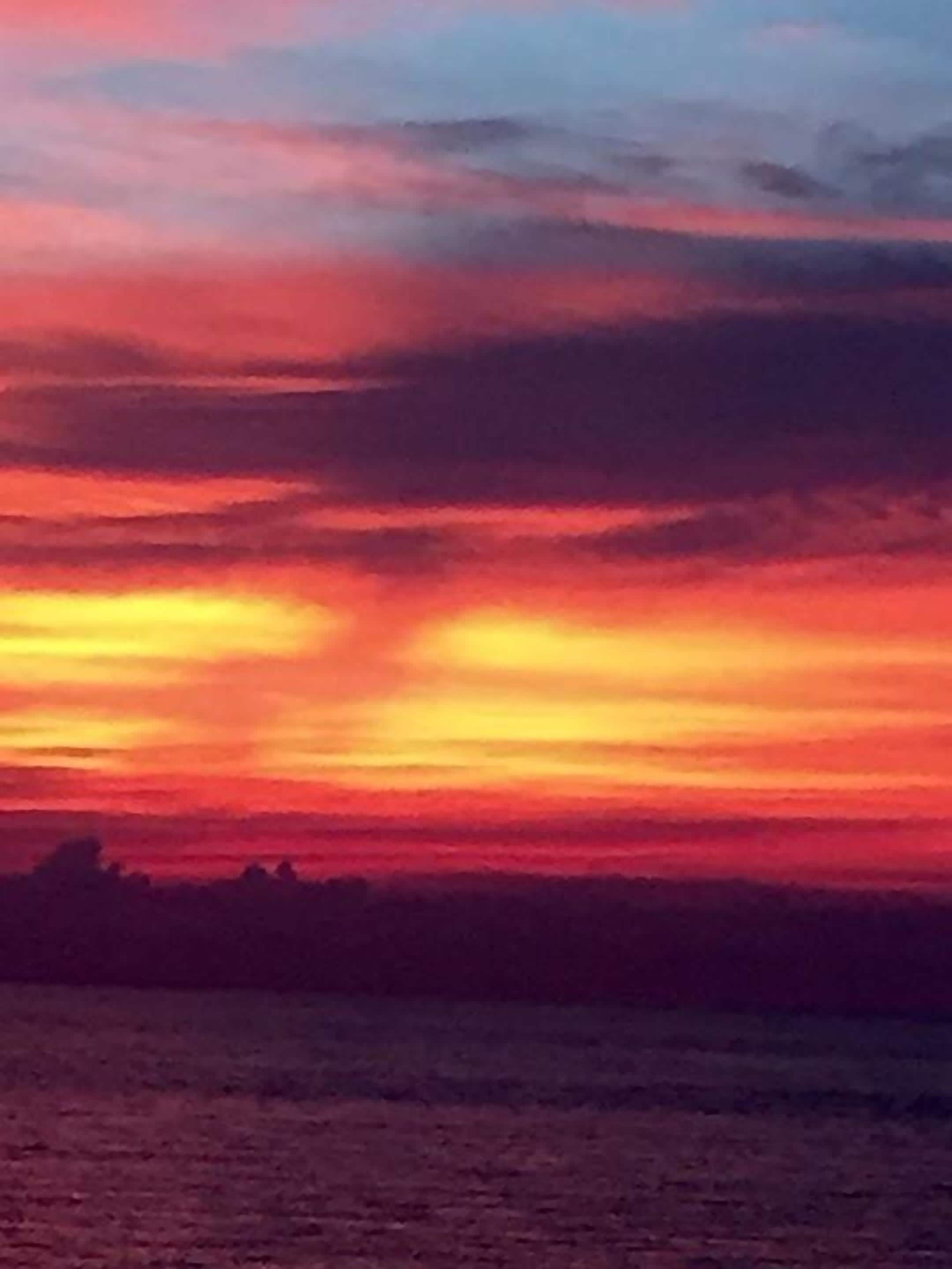 A sunset over a body of water with a silhouette of trees in the distance.