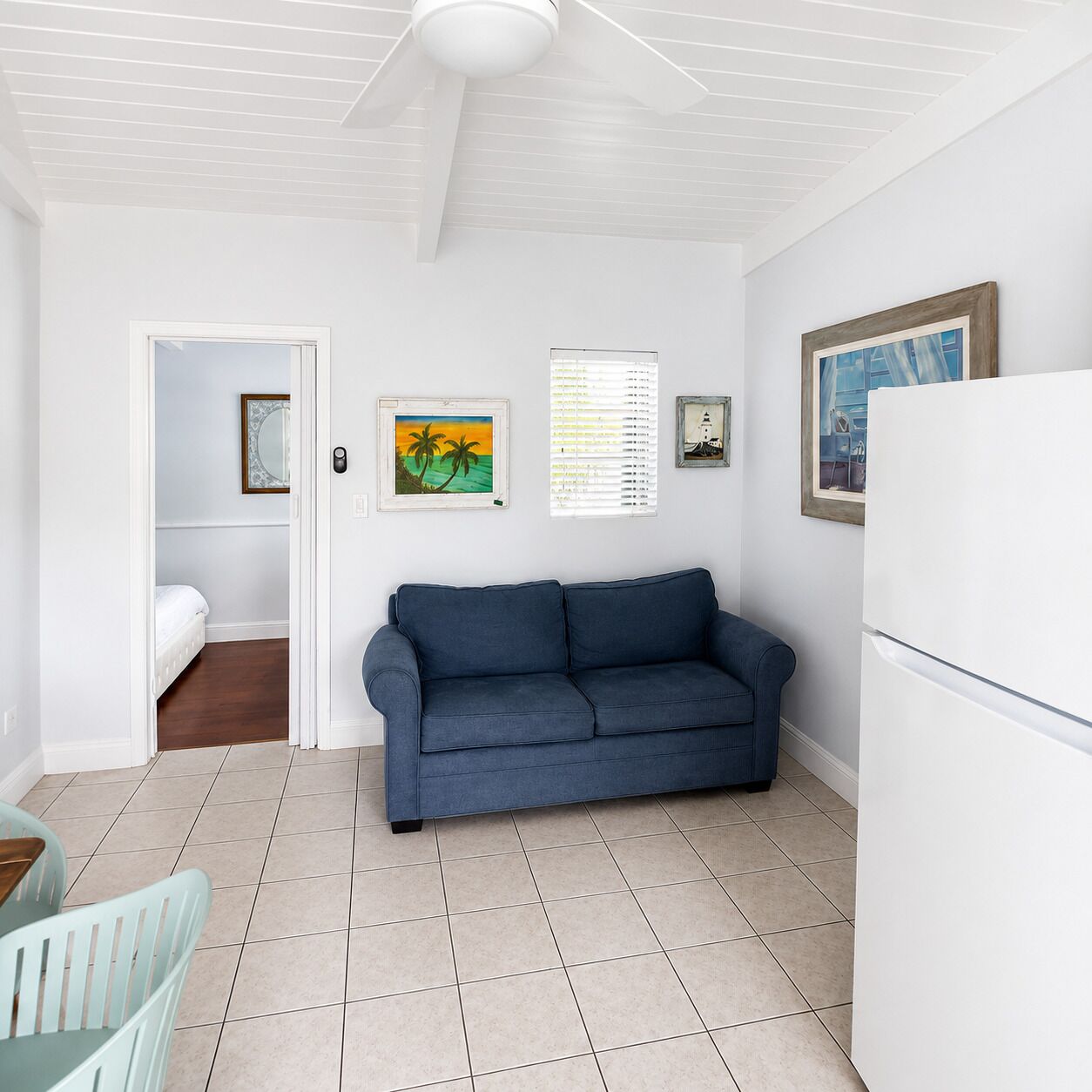 A room with a blue sofa, a white refrigerator, and a dining area with a table and chairs.