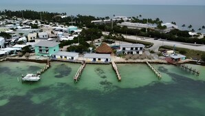 An aerial view of a coastal resort with multiple buildings, a dock with boats, and a clear view of the ocean.
