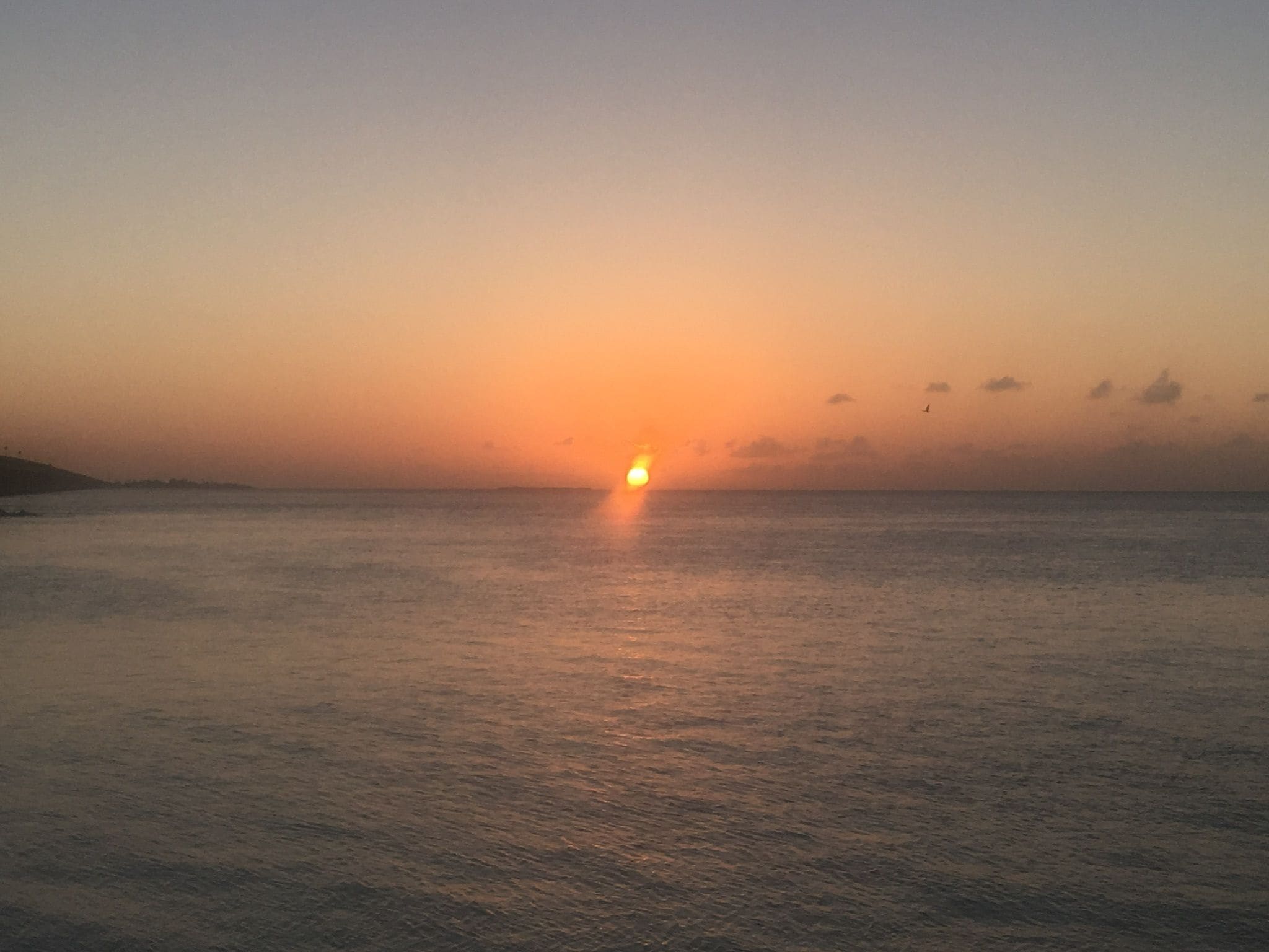 A sunset over a calm sea with a distant shoreline.