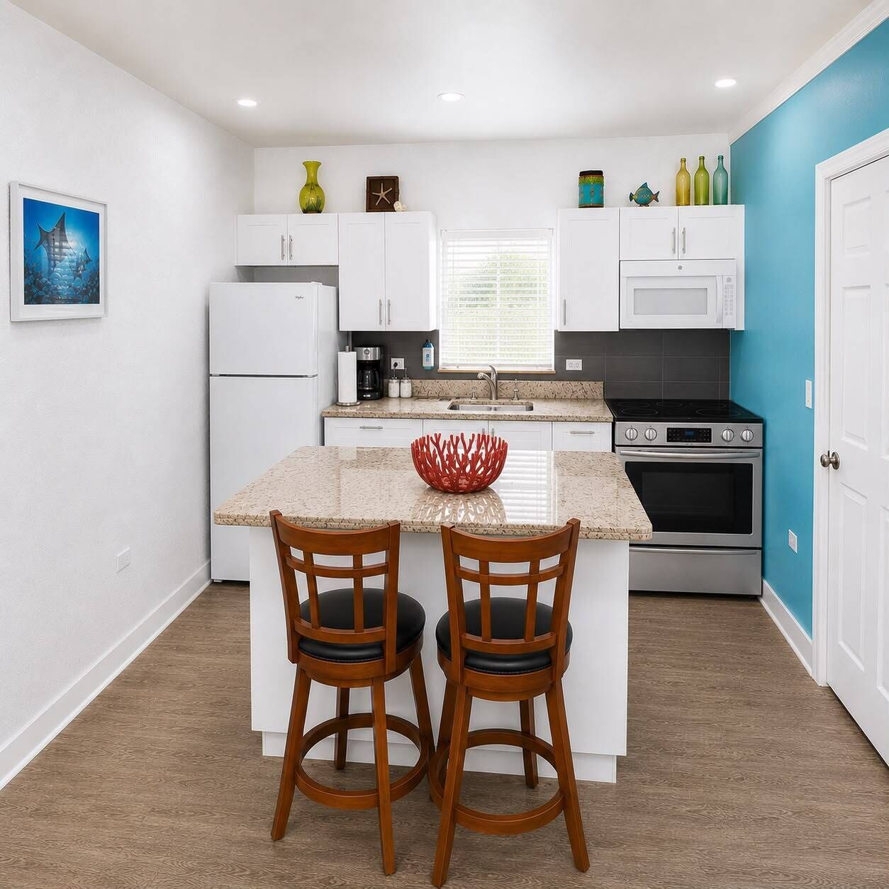 A modern kitchen with white cabinets, a central island, two wooden chairs, a red decorative bowl, and a microwave.