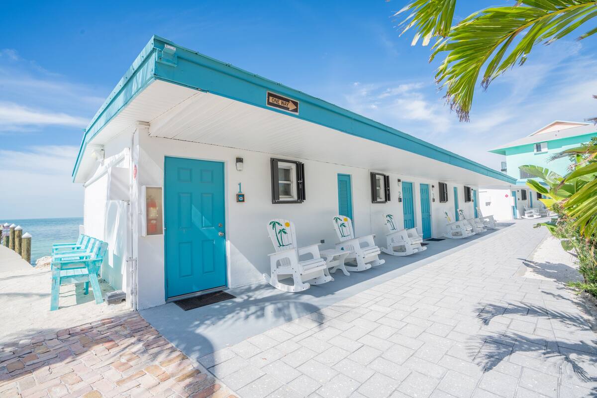 A beachfront building with a one-way sign, white walls, blue doors, and white rocking chairs along the side.