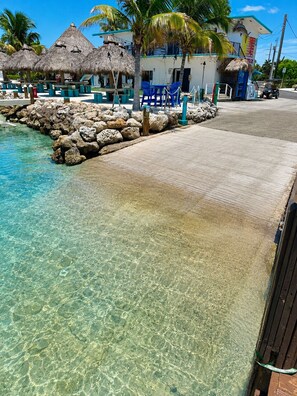 A clear tropical pool with a rocky edge, a thatched-roof building, and a paved walkway. - Edgewater Lodge (Long Key)