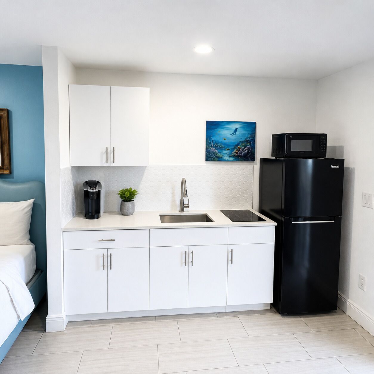 Cocina compacta con armarios blancos, un refrigerador negro, microondas y cafetera.