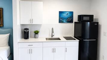 Cocina compacta con armarios blancos, un refrigerador negro, microondas y cafetera.