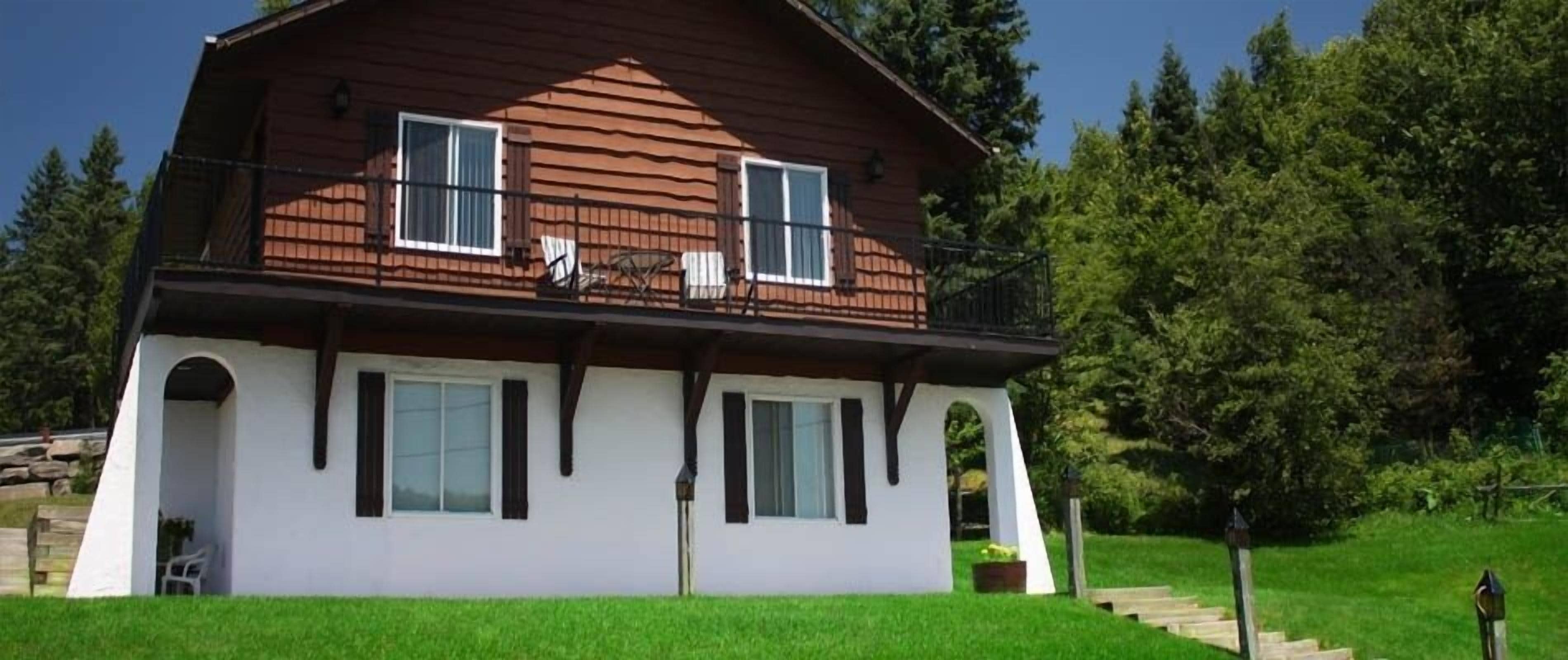 A two-story wooden house with a balcony, white exterior walls, and a small porch area.