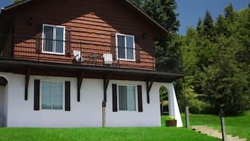 A two-story wooden house with a balcony, white exterior walls, and a small porch area.