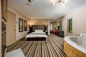 Habitación de hotel con una cama grande, baño independiente con bañera y vistas al exterior.