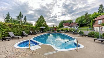 A swimming pool with lounge chairs and a hot tub, surrounded by greenery and houses.