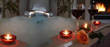 Uma área de spa com banheira, velas e uma rosa.