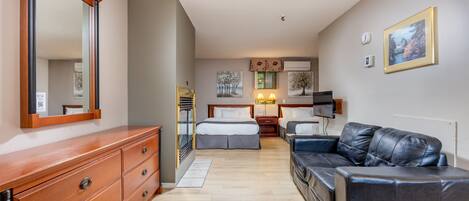 Habitación de hotel con tocador de madera, cama con cabecera, sofá de cuero negro y un espejo grande.
