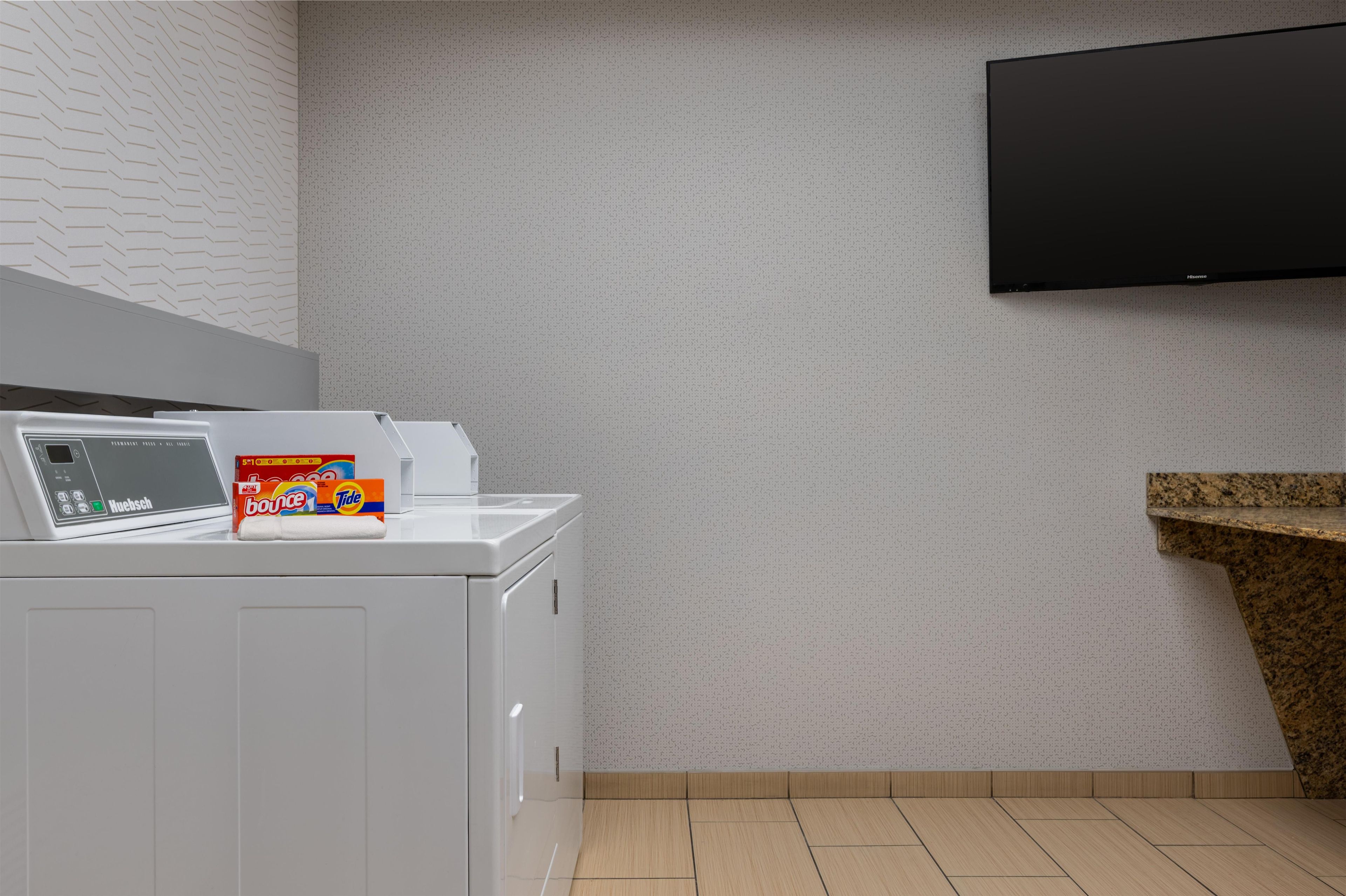 A laundry room with a front-loading washing machine, a wall-mounted television, and a granite countertop.