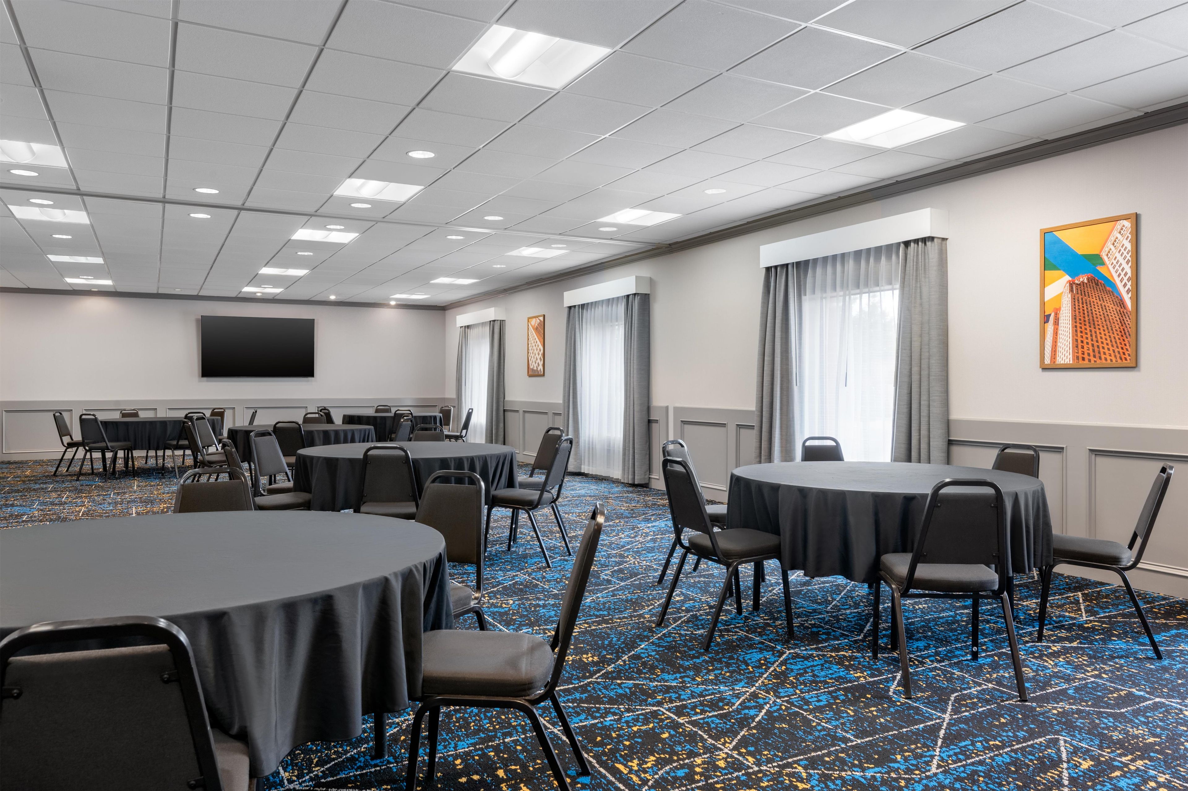 A conference room with round tables, chairs, a flat-screen TV, and a patterned carpet.
