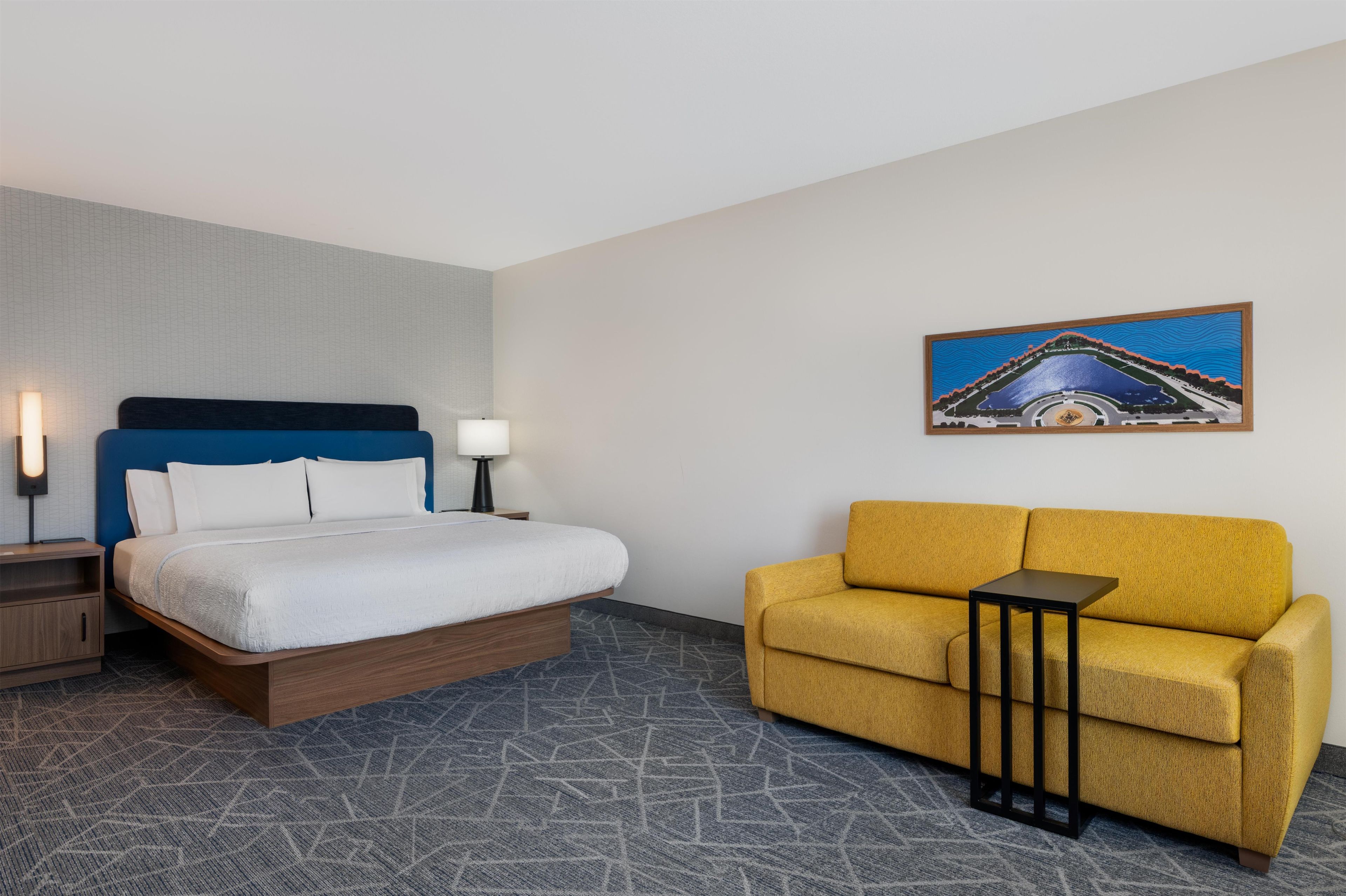 Una habitación de hotel con cama, sofá, una mesita y un cuadro en la pared.