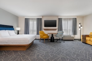 A hotel room with a bed, two chairs, a table, a flat-screen TV, and a heater.
