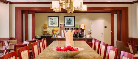 A long conference table with chairs, a chandelier, and a fruit bowl in the center.