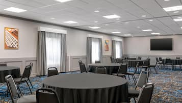 Un salón de conferencias con mesas redondas, sillas, un televisor de pantalla plana grande y obras de arte en las paredes.