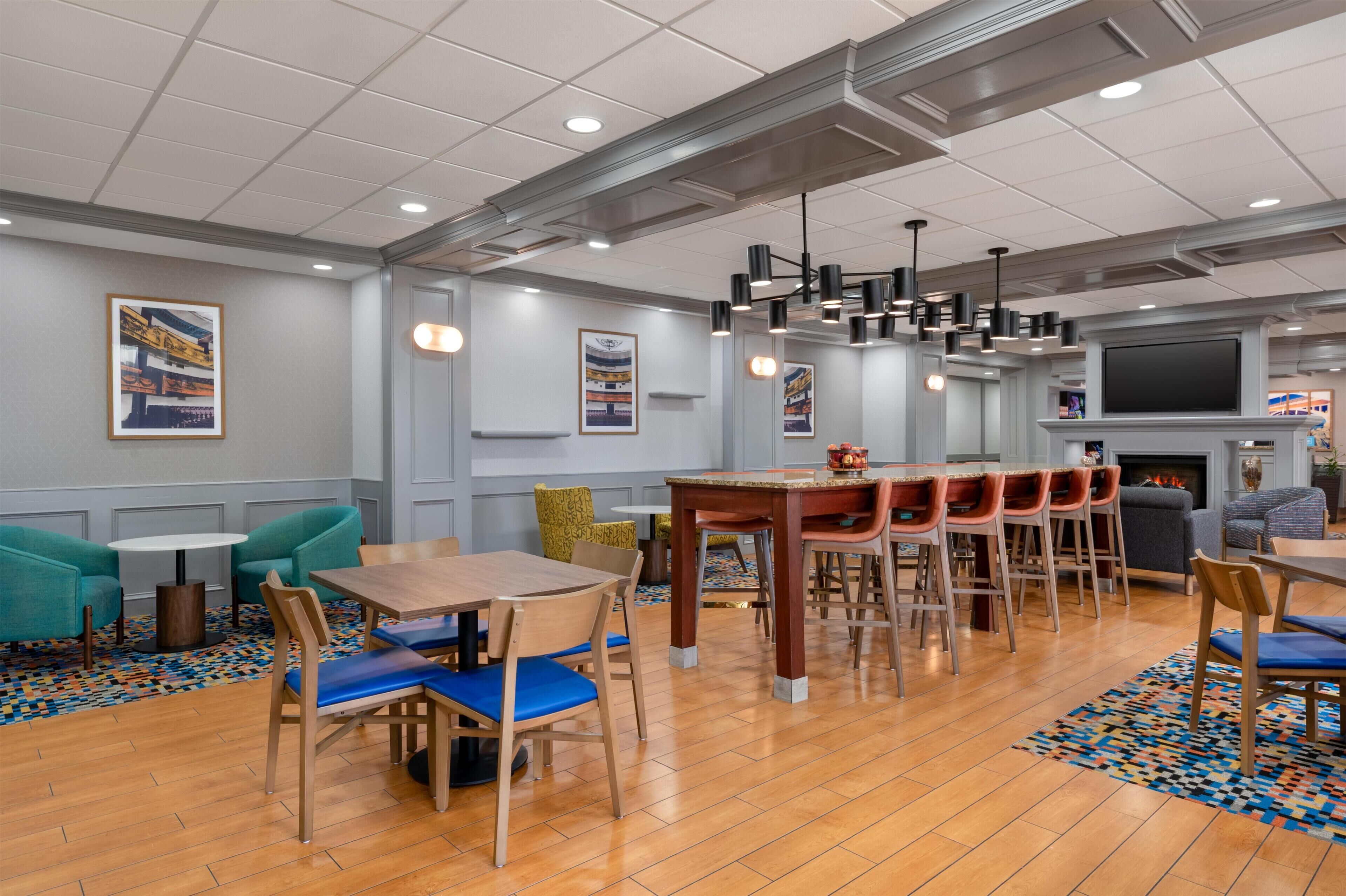 Un espace repas moderne avec des tables et des chaises en bois, un bar avec des tabourets et une cheminée.