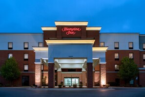 A Hampton Inn hotel with a modern facade, a prominent neon sign, and a well-lit entrance.