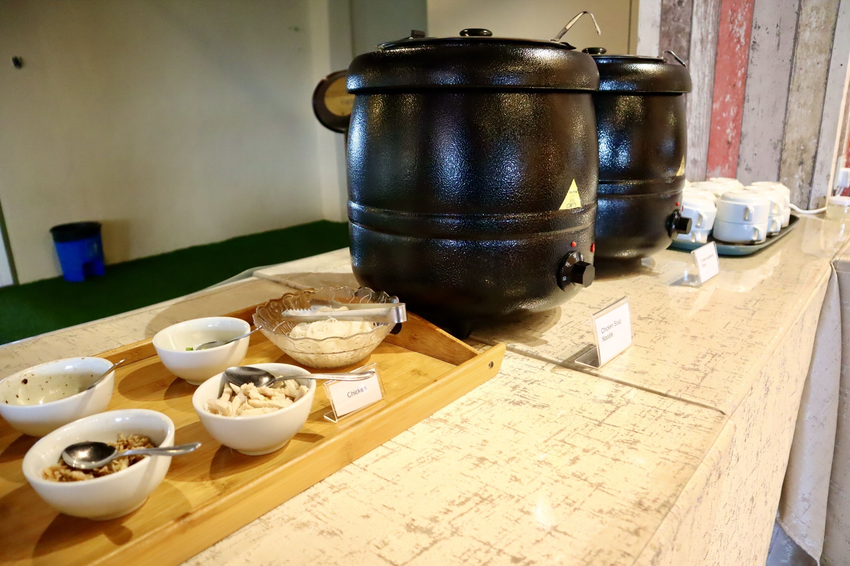 Ein reichhaltiges Buffet mit verschiedenen Schalen voller Speisen auf einer Holzwage, einem großen schwarzen Topf und einem Schild mit der Aufschrift 'Chill Side Noodle'.