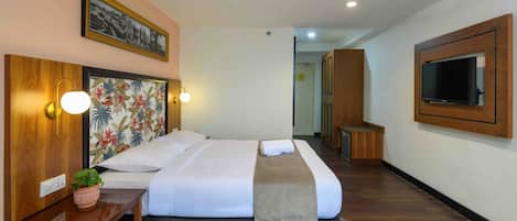A hotel room with a large bed, a wooden headboard, a wall-mounted TV, and a small table with a plant.