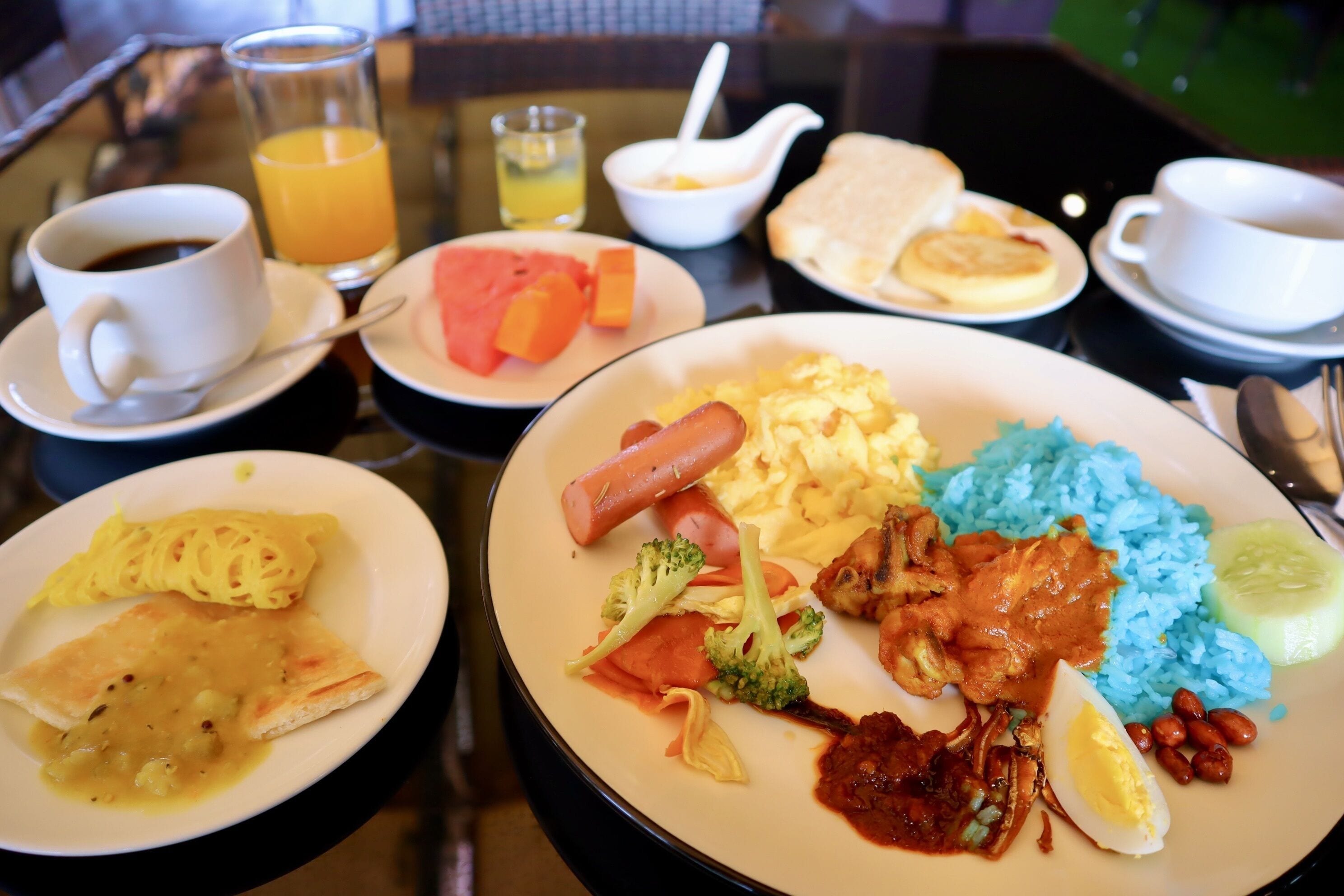 A table with breakfast plates containing eggs, sausages, rice, and vegetables. There are also cups of coffee and juice.