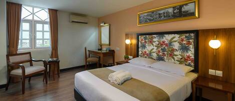 A hotel room with a large bed, a desk, a chair, and a window with curtains.
