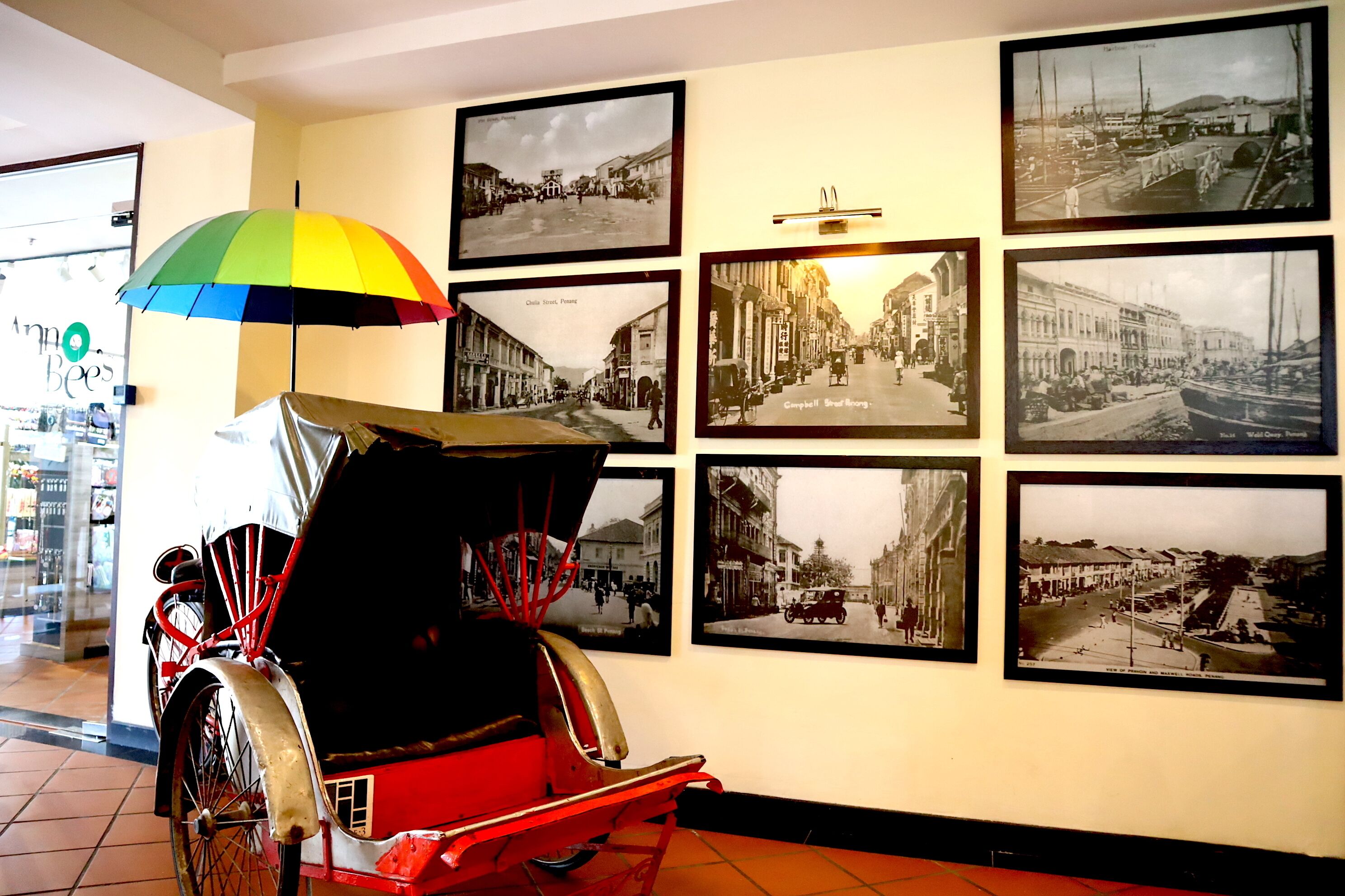 A vintage rickshaw with a colorful umbrella parked in a room with walls adorned with black and white historical photographs.