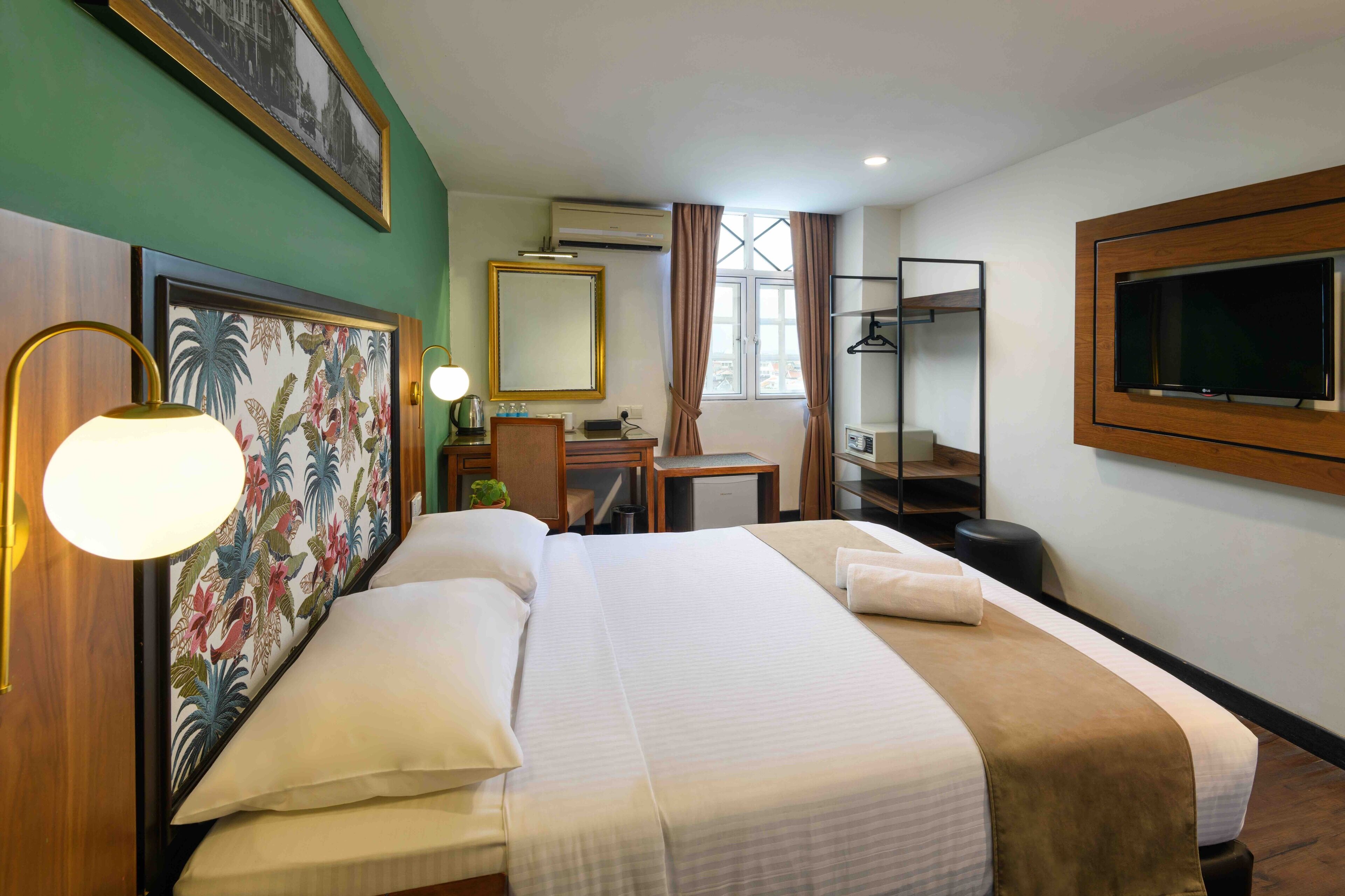 A hotel room with a bed, a desk, a chair, a television, and an air conditioning unit.