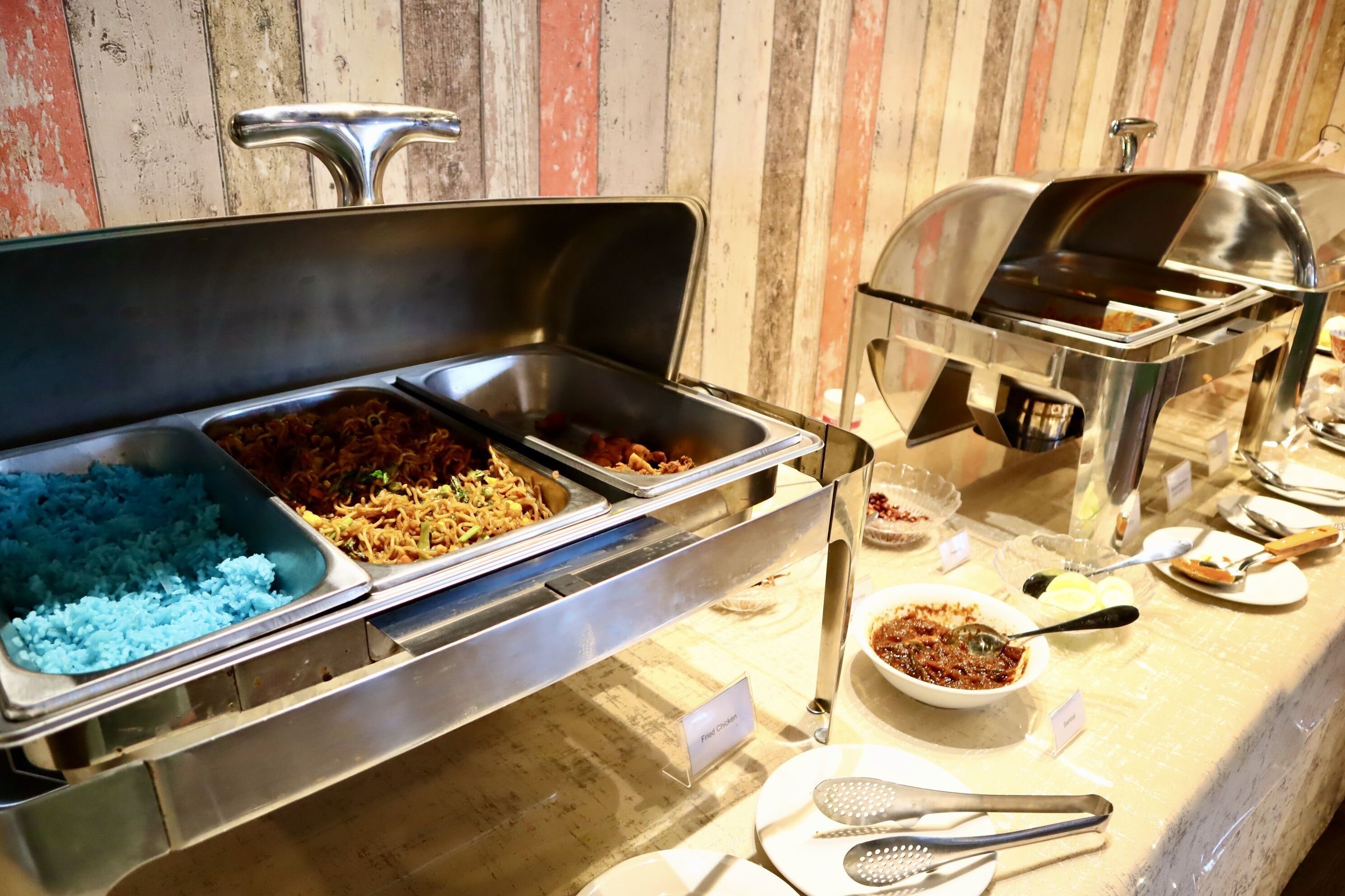 A buffet with various food options, including blue rice, fried chicken, and a bowl of sauce.