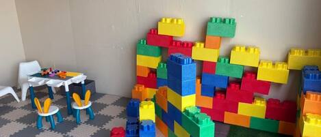 Un espace de jeux avec une table et des chaises, ainsi qu’un mur orné de blocs de construction colorés.