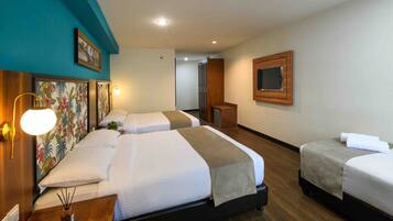 Una habitación de hotel con tres camas, un cabecero de madera, un televisor y un cuadro en la pared.