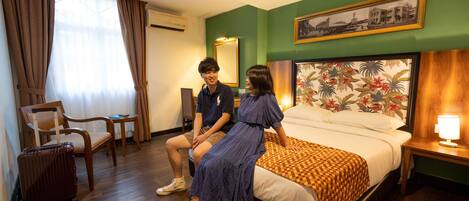 A hotel room with a bed, a chair, a table, and a suitcase.
