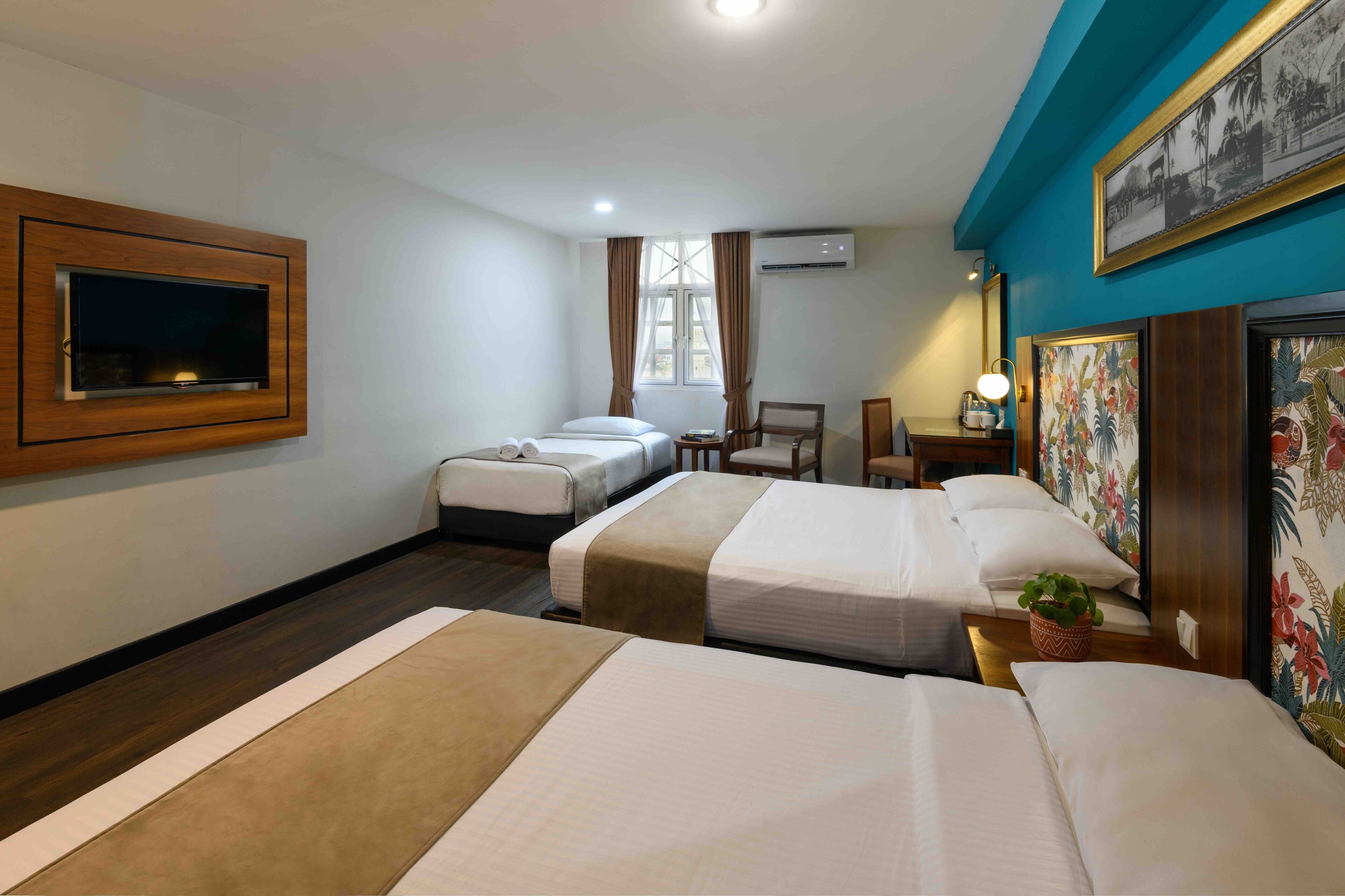 A hotel room with two beds, a TV mounted on the wall, a desk with a chair, and a window with curtains.