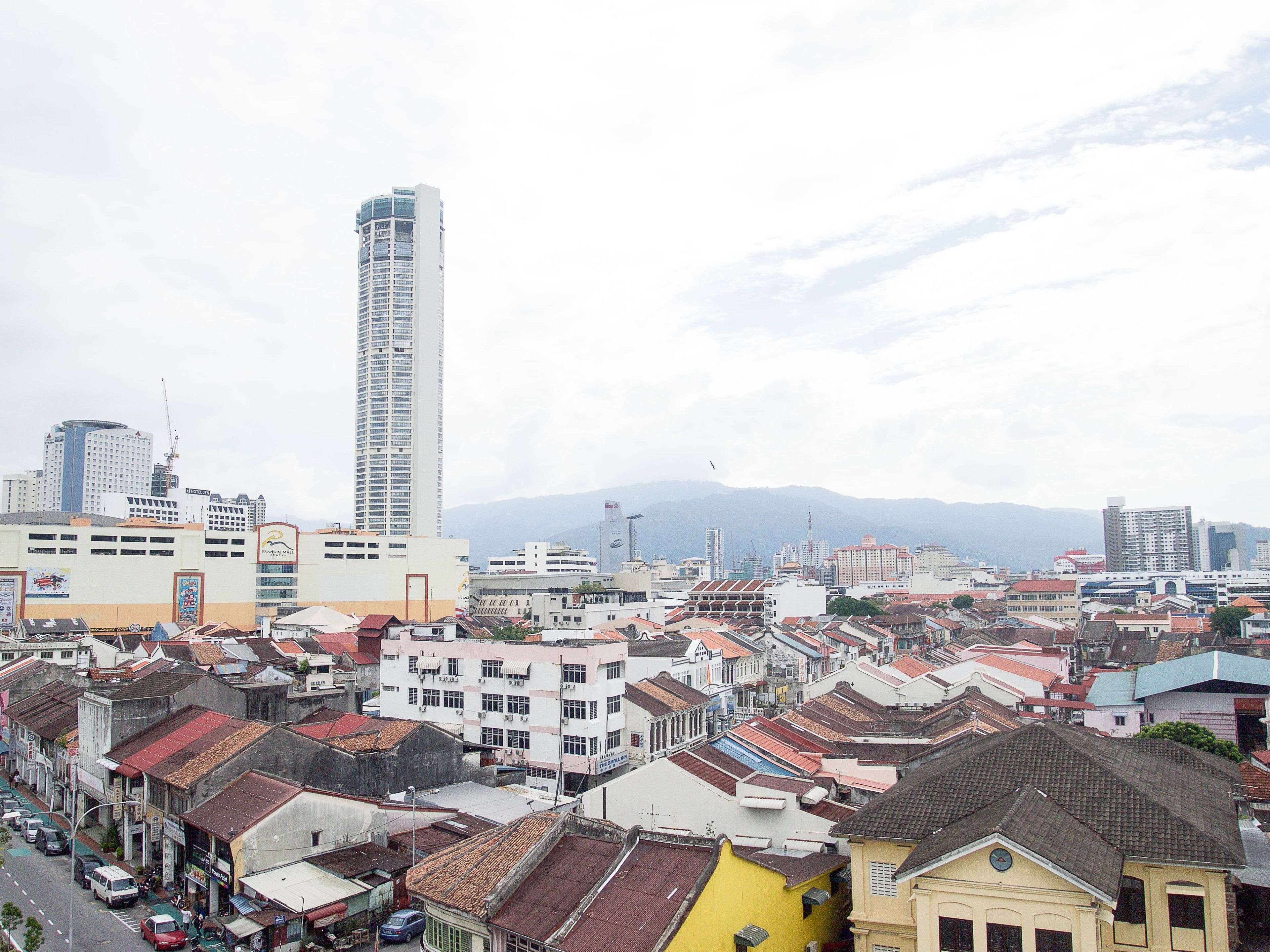 A cityscape with a prominent tall building, a mix of residential and commercial buildings, and a mountainous backdrop.