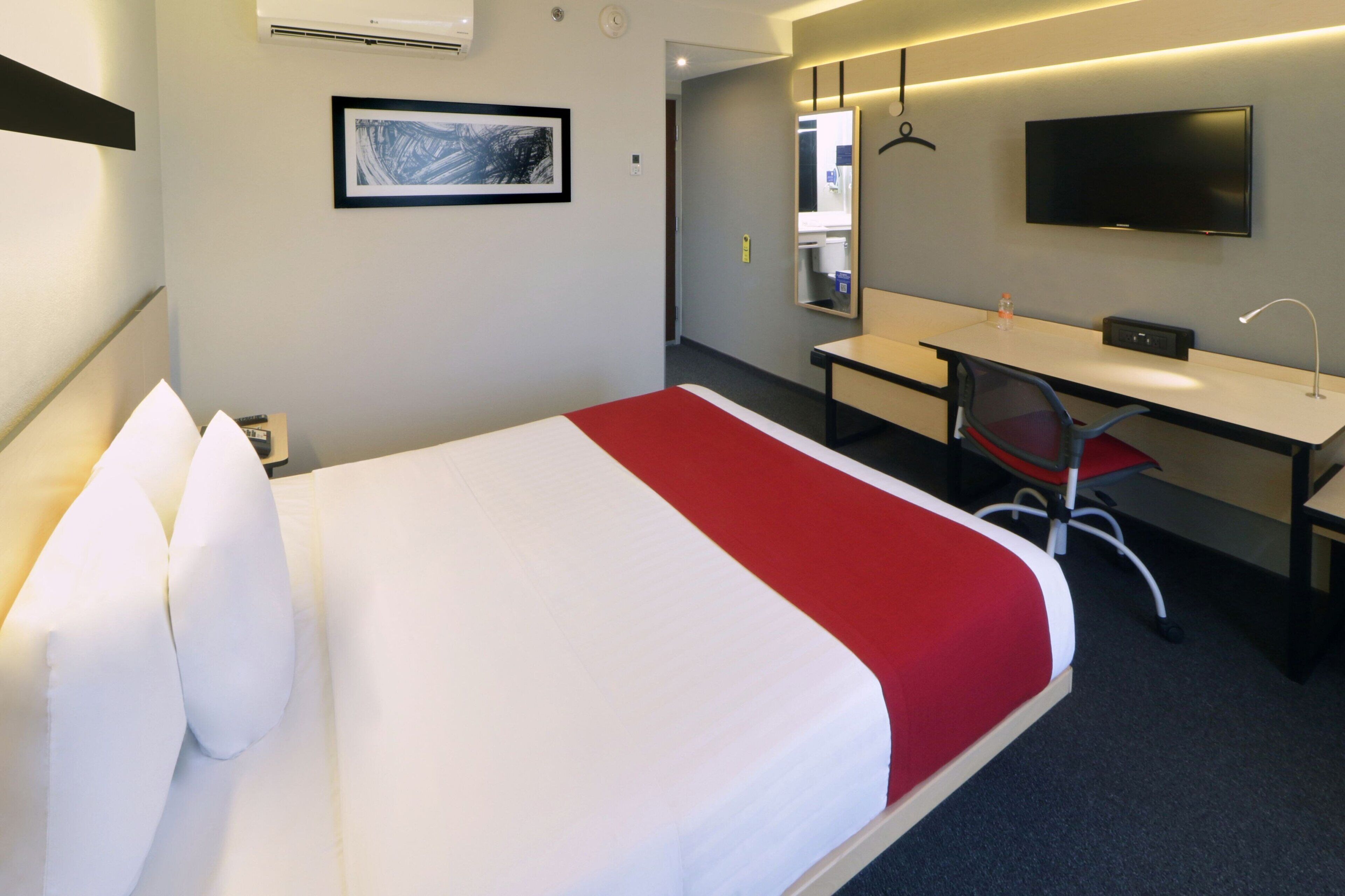 Una habitación de hotel con una cama, un escritorio, una silla, un televisor y un espejo.