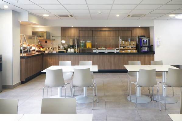 A modern dining area with white tables and chairs, a counter with food and drink dispensers, and a microwave above it. - City Express by Marriott Tijuana Insurgentes (Tijuana)