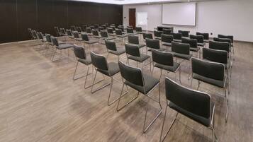 Un salón de conferencias con filas de sillas, una pizarra y una pantalla de proyección.