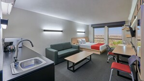 Habitació d'hotel moderna amb cuina sencera, sofà, llit, taula de dinar i vista al paisatge del desert.