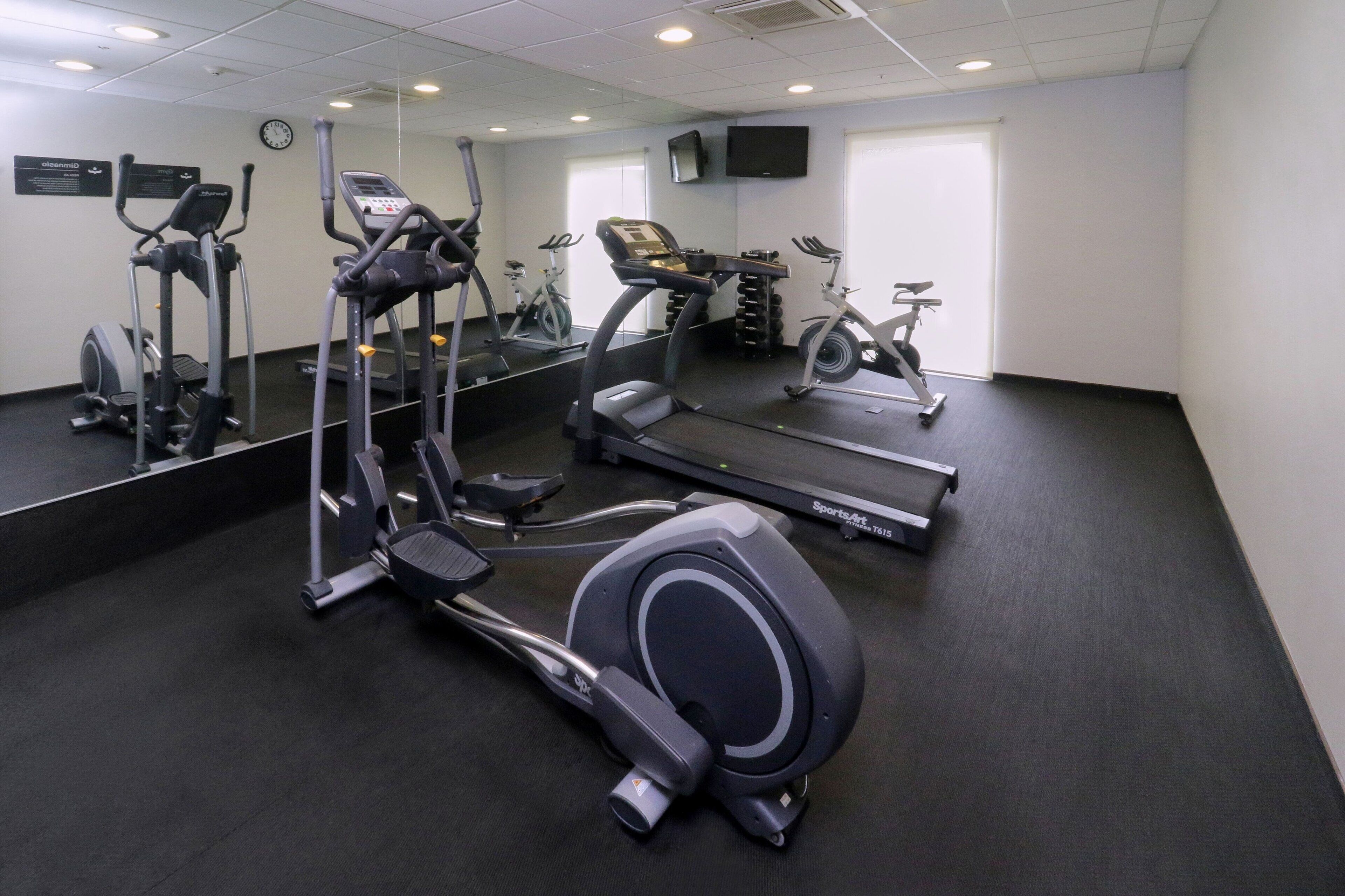 Un gimnasio con diversos equipos de ejercicio, incluyendo cintas de correr y elípticas.