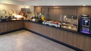 Un área de bufé con diferentes opciones de comida, un microondas y un dispensador de bebidas.