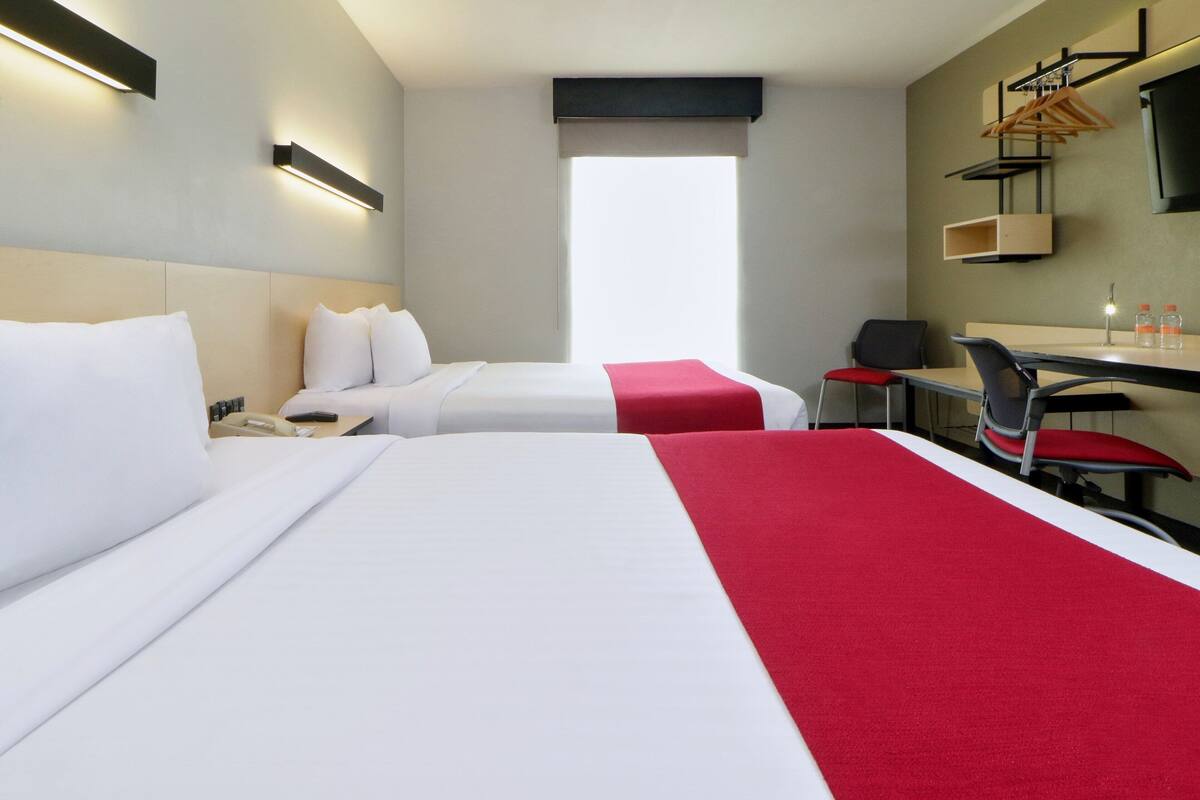 A hotel room with two beds, a desk, a chair, a TV, and a window.