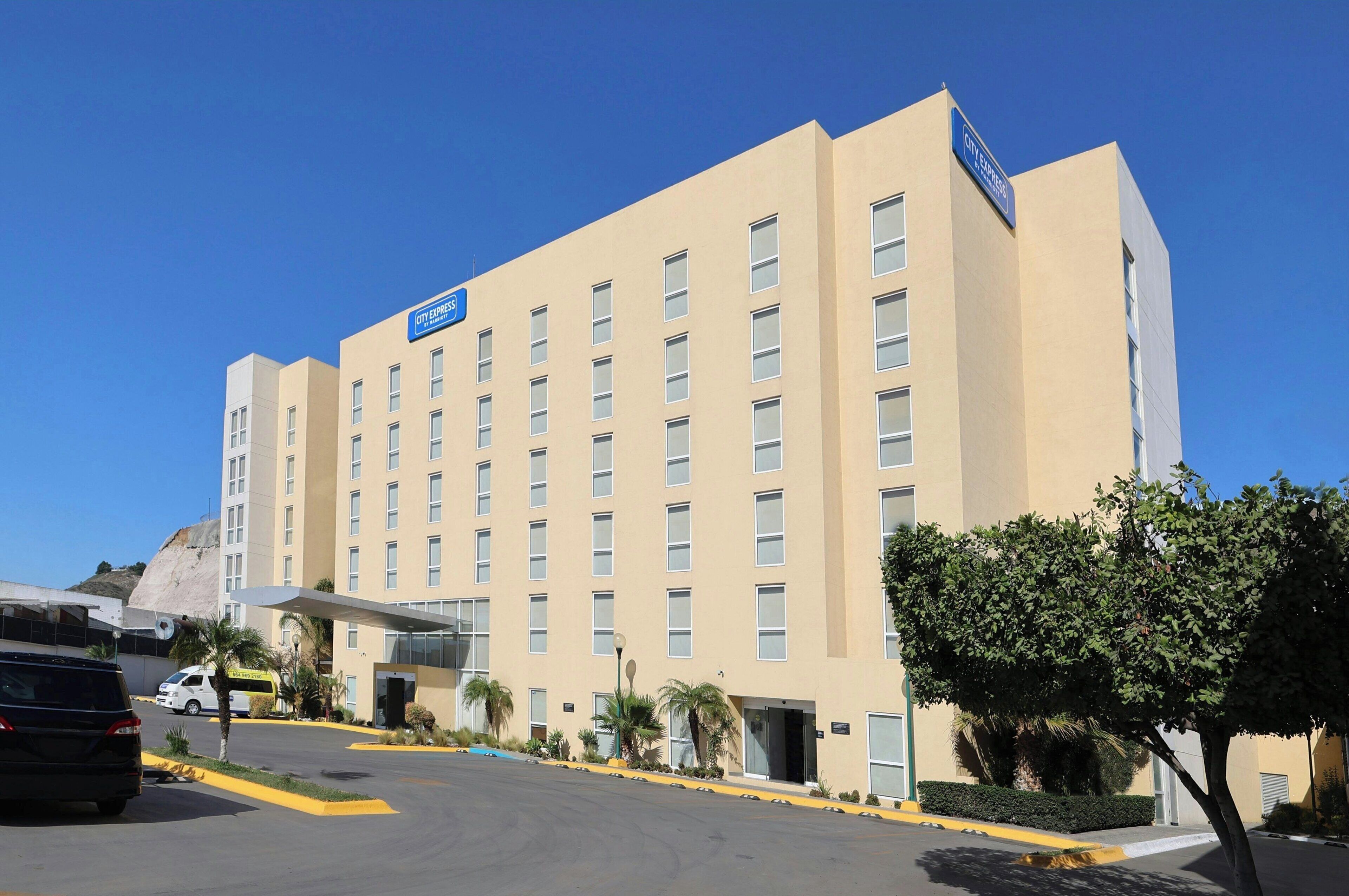 Un hotel de varios pisos con fachada plana, un llamativo letrero que dice 'CITY CENTER', y un estacionamiento con algunos vehículos.