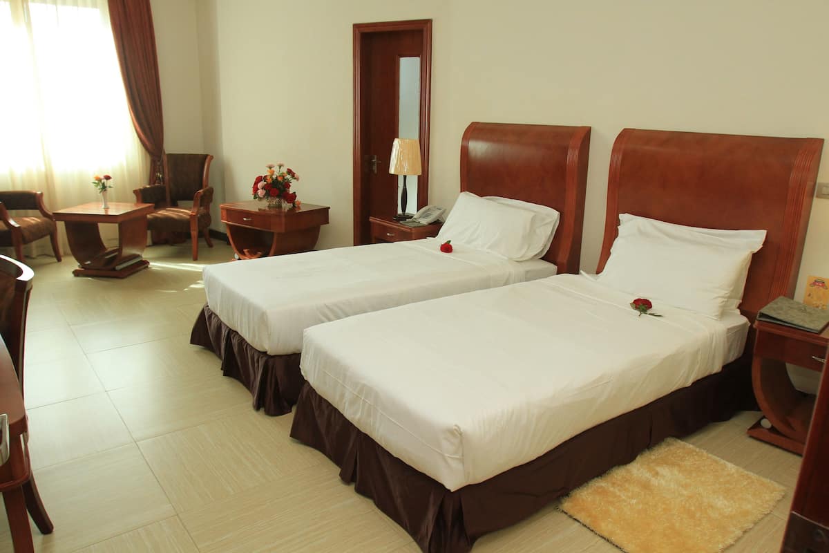 A hotel room with two beds, a desk, a chair, a nightstand, and a mirror.