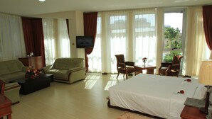 A hotel room with a bed, two sofas, a coffee table, a TV, and a window with curtains. - Aphrodite International Hotel (Addis Ababa)