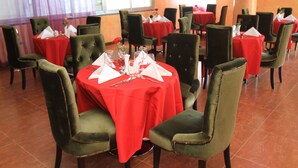 A restaurant with round tables covered in red tablecloths, green upholstered chairs, and neatly set dining tables with silverware and glassware. - Aphrodite International Hotel (Addis Ababa)
